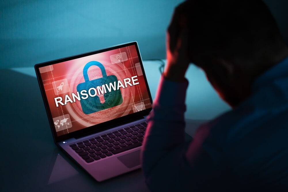 trauriger Mann sitzt vor dem Laptop mit dem Warnhinweis Ransomware